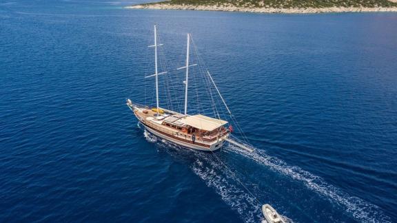 Aerial view of the 4-cabin Gulet Optimist sailing on blue waters near a rocky coastline.