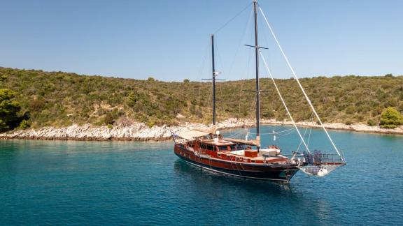 Die Gulet Pacha liegt ruhig vor Anker in einer Bucht, umgeben von türkisfarbenem Wasser und grüner Natur.