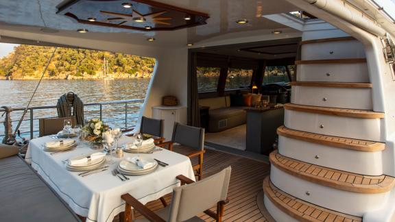 Auf der Perdue in Fethiye sind ein gedeckter Esstisch und der Zugang zum Salon auf dem Achterdeck zu sehen.