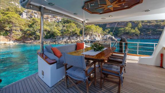 Auf der Perdue in Fethiye sind ein Esstisch und ein gemütlicher Sitzbereich auf dem überdachten Deck zu sehen.