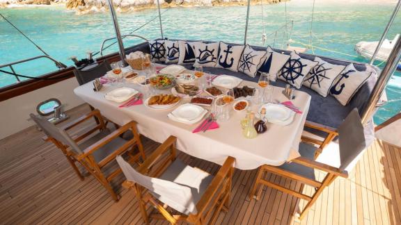 Among Fethiye yacht rental options Queen Alin aft deck shows dining table with rich service and seating area.