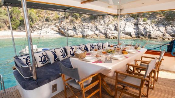 Among Fethiye yacht rental options Queen Alin aft deck shows dining table and seating area with sea view.