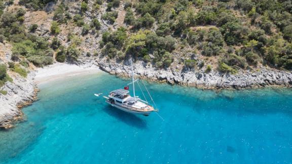 Among Fethiye yacht rental options Queen Alin is anchored in a calm clear bay with natural coastline view.