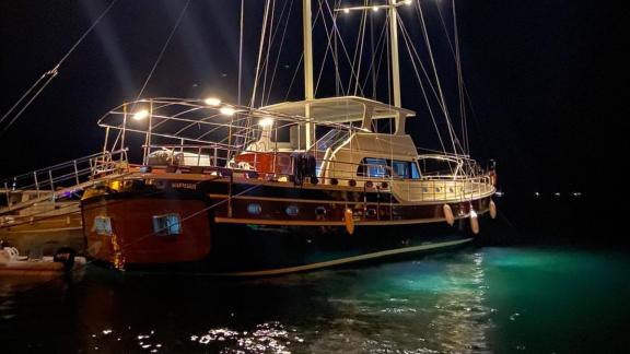 The gulet Rose Sah is anchored under night lights, reflecting on the water.