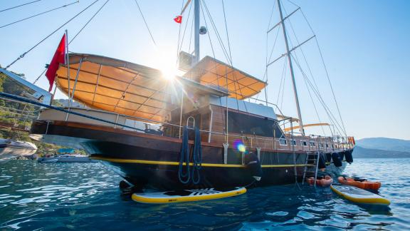 The Gulet Rüya basking in sunlight, anchored with two SUP boards and kayaks in calm waters.