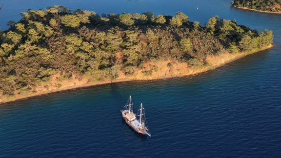 The Gulet Rüya anchored by a wooded island in clear blue waters, a peaceful oasis.