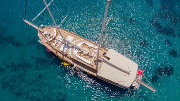 Aerial view of a large sailing yacht anchored on crystal-clear, turquoise-coloured water.