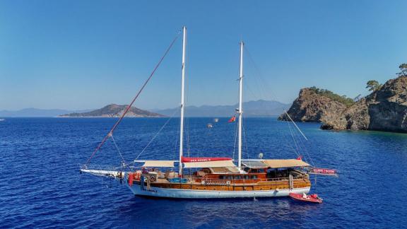 The gulet Sea Angel 2 is peacefully anchored in a tranquil cove, surrounded by blue waters.