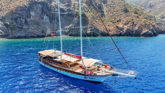 Die Gulet Sea Angel 2 liegt vor Anker im türkisfarbenen Wasser in der Nähe einer grünen Bucht.