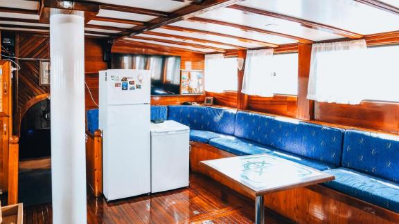 The saloon of gulet Sea Angel 2 features a cozy seating area, a refrigerator, and wooden decor.