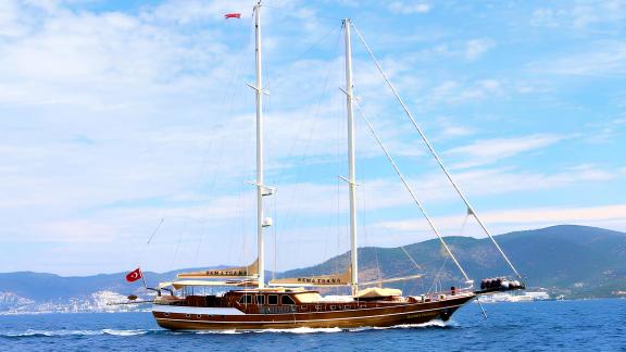 The gulet Sema Tuana from Bodrum with 6 cabins, elegant and classic, in front of a coastal landscape.