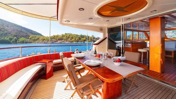 In Göcek gulet charter option Serenity 86 aft deck with large dining table seating area and nature view offering comfort