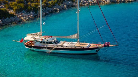 In Göcek luxury gulet charter option Serenity 86 anchored in turquoise water with spacious deck and sunbathing area visi