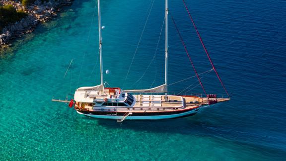 In Göcek gulet charter option Serenity 86 bird eye view in turquoise water with spacious deck and sunbathing area visibl