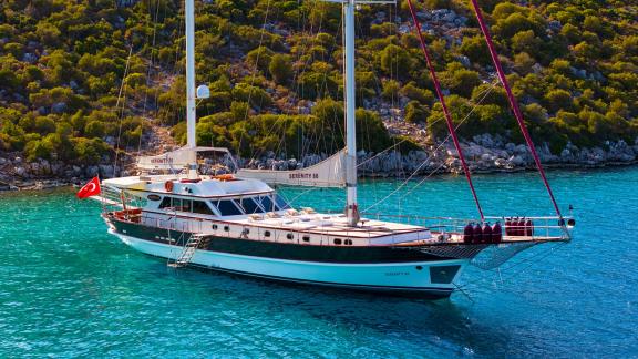 In Göcek gulet charter option Serenity 86 side view in clear water with spacious deck and sunbathing area visible.