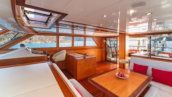 In Göcek gulet charter option Serenity 86 interior salon with seating area table and panoramic sea view visible.