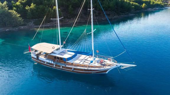 Gulet Seven 1 is peacefully anchored in turquoise waters in a forested bay.