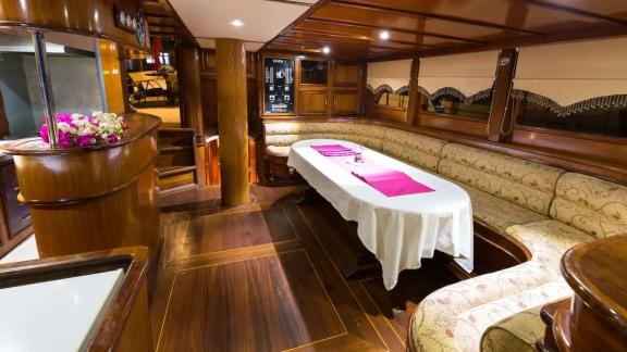 The interior of Gulet Seven 1 features wooden details, a long table, and comfortable seating area.