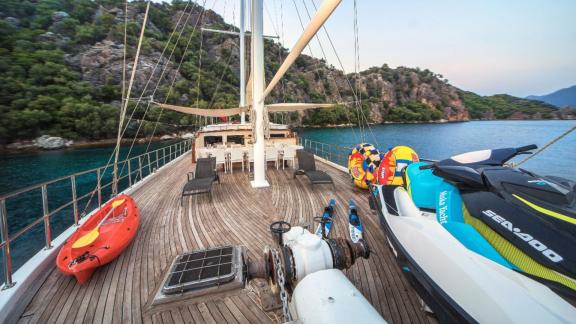 Deck einer Gulet mit Wassersportausrüstung vor einer Küste.