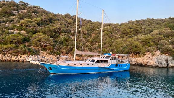 The Gulet Simi anchored off a picturesque coastline in the Mediterranean, surrounded by lush greenery.