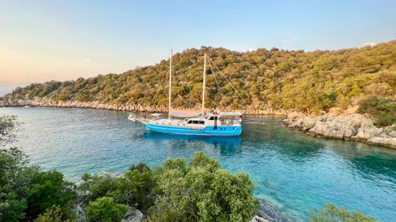 The Gulet Simi anchored in a tranquil cove surrounded by green hills in the Mediterranean, perfect for relaxation.