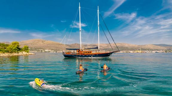 The gulet Smart Spirit is anchored in calm coastal waters while three people on jet skis ride in the foreground.