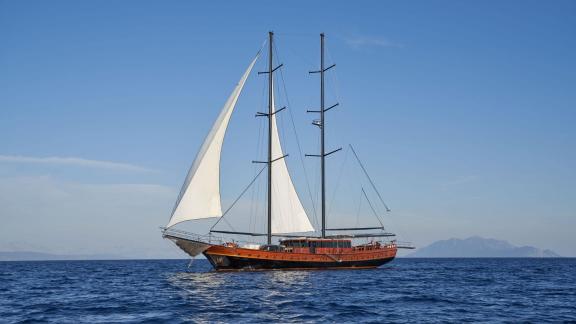 A large, elegant sailing yacht with white sails sails on a calm, blue sea under a clear sky.