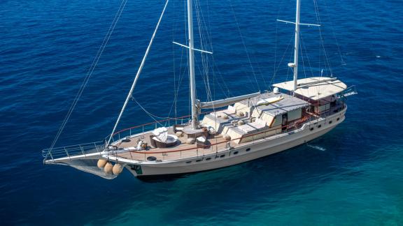 A spacious gulet with a sun deck and masts glides through deep blue waters.