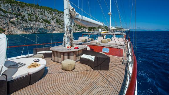 The luxurious deck of a gulet with seating, surrounded by clear water and rocky shores.