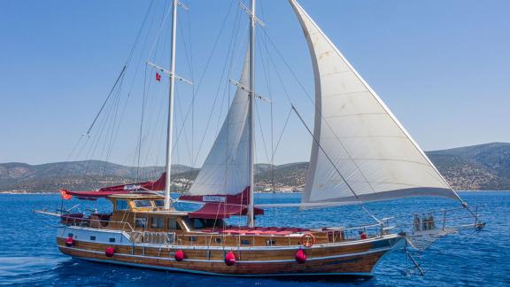 Wunderschöne traditionelle Gulet mit weißen Segeln vor der malerischen Küste von Bodrum. Perfekt für Segelabenteuer.