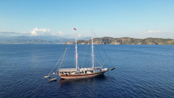 The gulet Tarkan 5 sails in the calm waters of Fethiye, surrounded by a picturesque coastal landscape and under clear sk