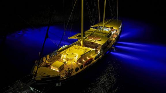 Die Gulet Tarkan 5, beleuchtet bei Nacht vor Anker in Fethiye, mit blauem Unterwasserlicht und elegantem Deck.