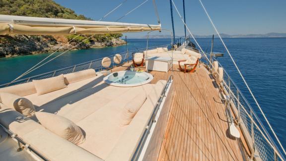 The luxurious deck of the gulet Tarkan 5 in Fethiye, with comfortable seating, a whirlpool and surrounded by clear, turq