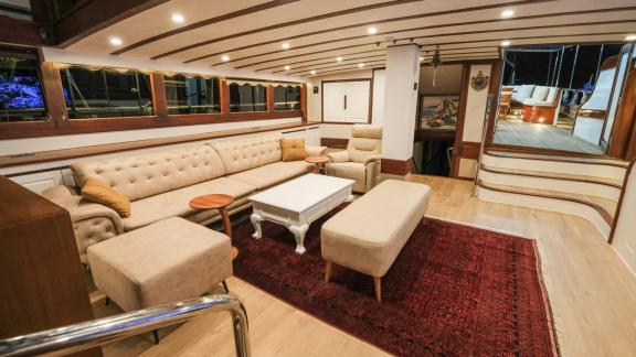 The cosy saloon of the Gulet Tarkan 5, furnished with a large sofa, armchairs, a carpet and stylish wooden accents.