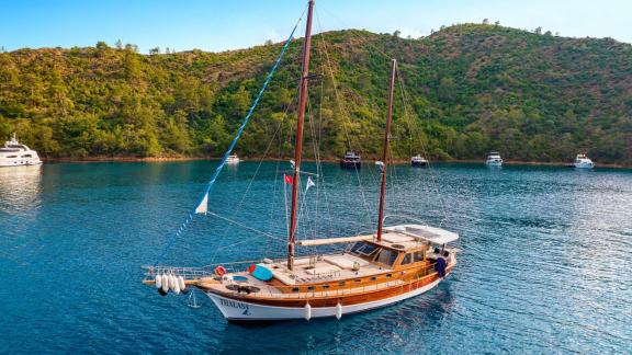 Gulet Thalasa anchored in a serene Turkish bay with green hills in the background.