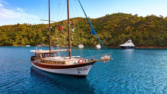 Die Gulet Thalasa gleitet durch türkisfarbenes Wasser, umgeben von grünen Hügeln und anderen Yachten.