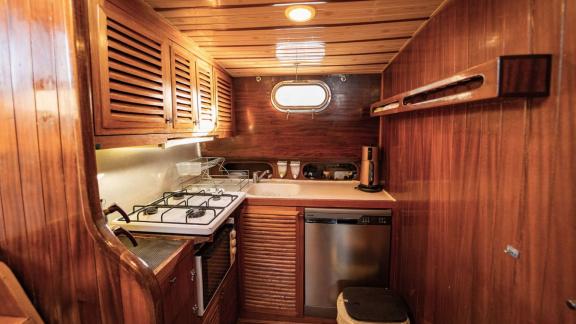 Interior view of the compact kitchen on Gulet Thalasa with stove, sink, and wooden cabinets.