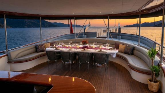 In Marmaris Gulet chartern Option Tosca Achterdeck mit Tisch und Meerblick für entspanntes Abendessen sichtbar.
