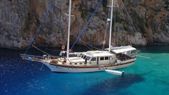 The Gulet Tufan 5 is anchored in a stunning turquoise bay, surrounded by rocky cliffs.