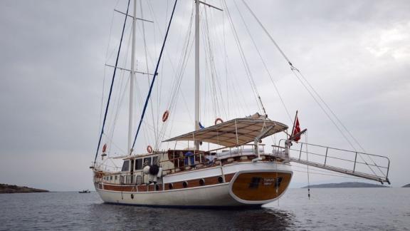 The Gulet Tufan 5 is anchored with a stern view, surrounded by calm waters and an overcast sky.