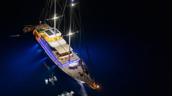 The gulet Vega is illuminated at night and lies at anchor in the dark water.