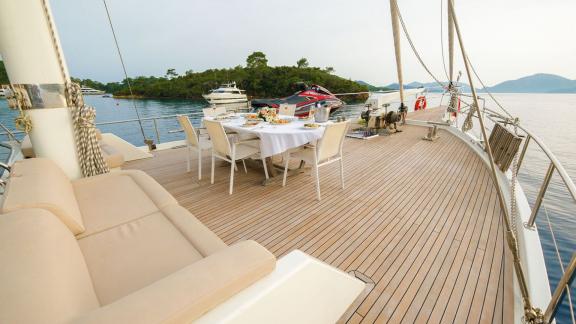 Deck of the gulet Vega with covered dining table and loungers, surrounded by calm water and other boats in the backgroun