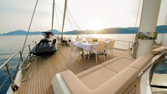 Deck of the gulet Vega at sunset with dining table, loungers and a jet ski.