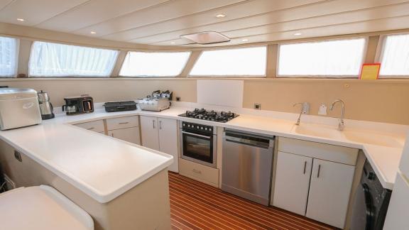 Modern kitchen of the Gulet Vega with full equipment, light-coloured cupboards and large windows.