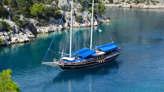 Elegante Gulet mit blauem Sonnenschutz, vor Anker in einer klaren, ruhigen Bucht.