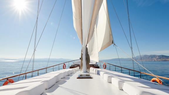 The foredeck of White Pearl gulet in Athens shows cushioned seating areas and raised sails while cruising.