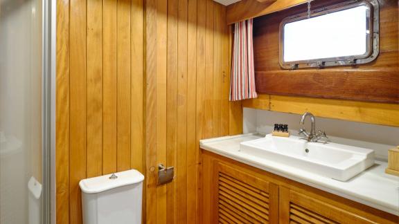 The wooden bathroom of White Pearl gulet in Athens includes a sink, toilet and storage cabinets.