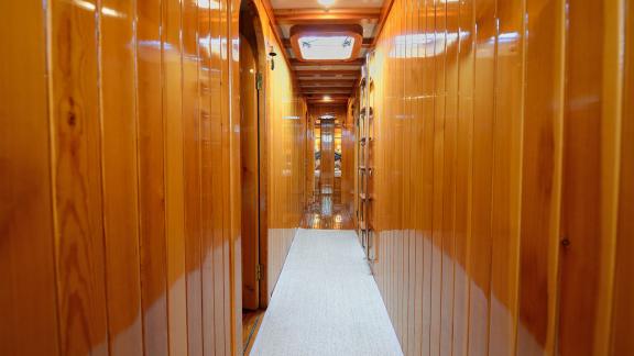 Elegant corridor of Gulet Xenos 2 in Bodrum with polished wood paneling and soft carpet.