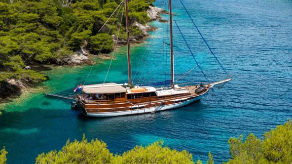 Die Gulet Eleganza liegt in türkisfarbenem Wasser umgeben von grünen Wäldern für einen erholsamen Urlaub.
