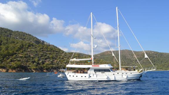 Die Gulet Gül Sultan, ein weißes Segelboot mit zwei Masten, liegt vor Anker auf ruhigem blauen Wasser.